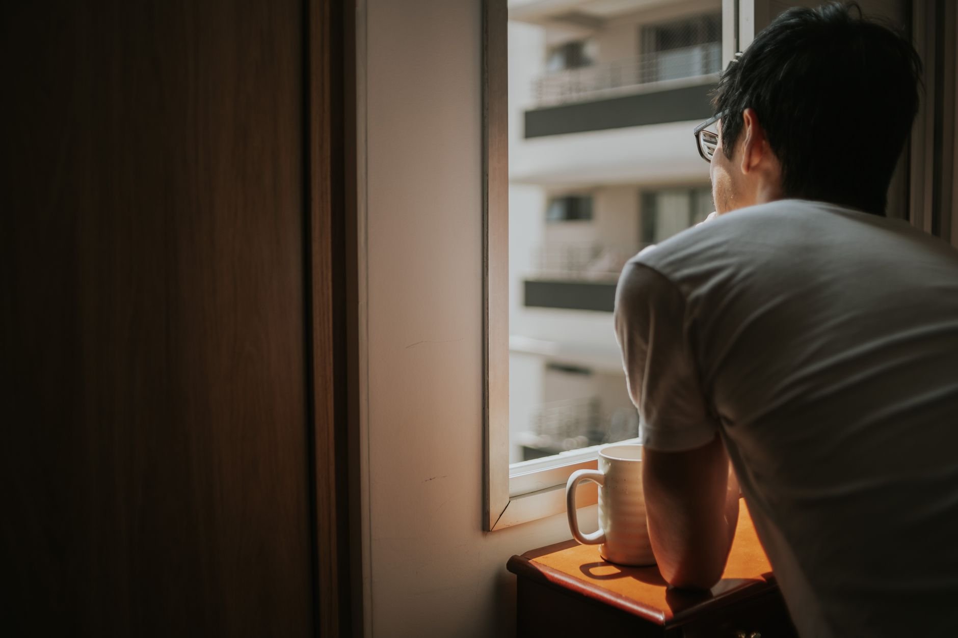 A man thoughtfully looks out a window, holding a mug — the weight of an unresolved dispute